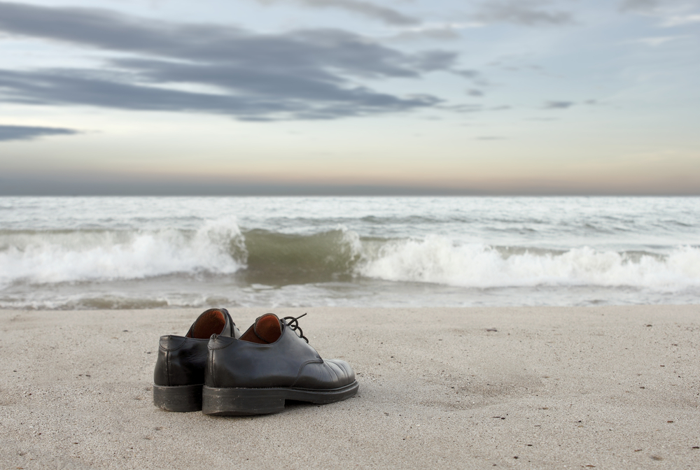 A pair of shoes sitting on the beach near water.